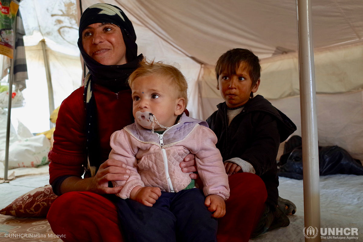 Naima, an internally displaced woman from Hawiga, smiles as she speaks to UNHCR staff with her youngest and eldest sons, Mohammed and Emad, in Al-Alam camp