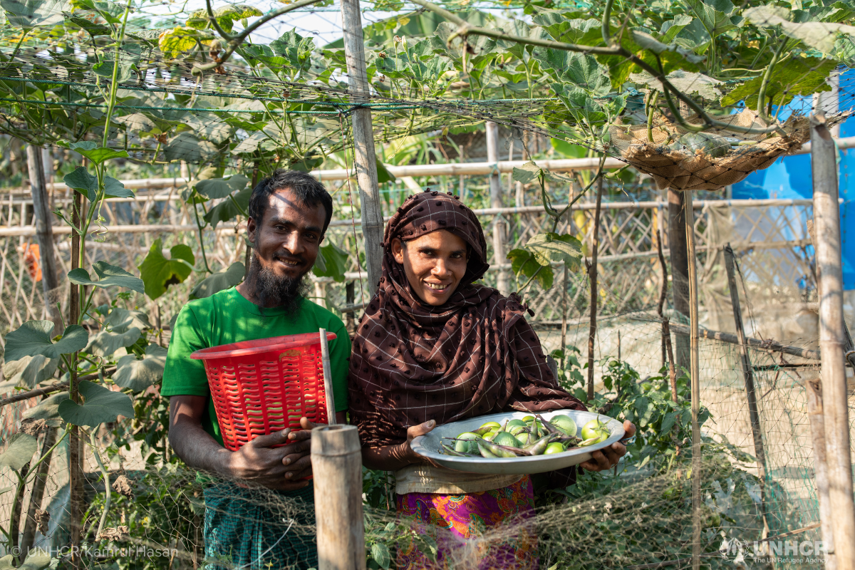 refugee couple holding a basket of tomatoes picked from their farm