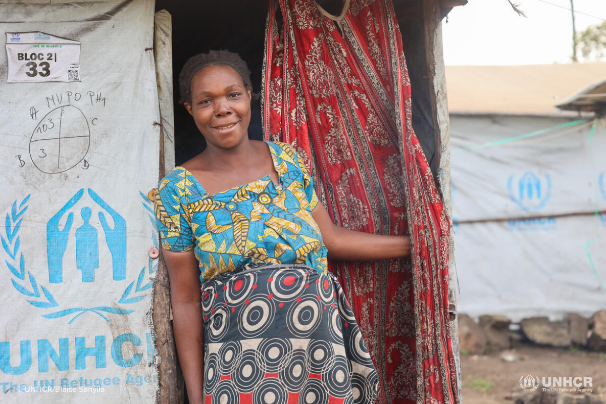 congolese refugee Furaha smiling outside of her UNHCR shelter