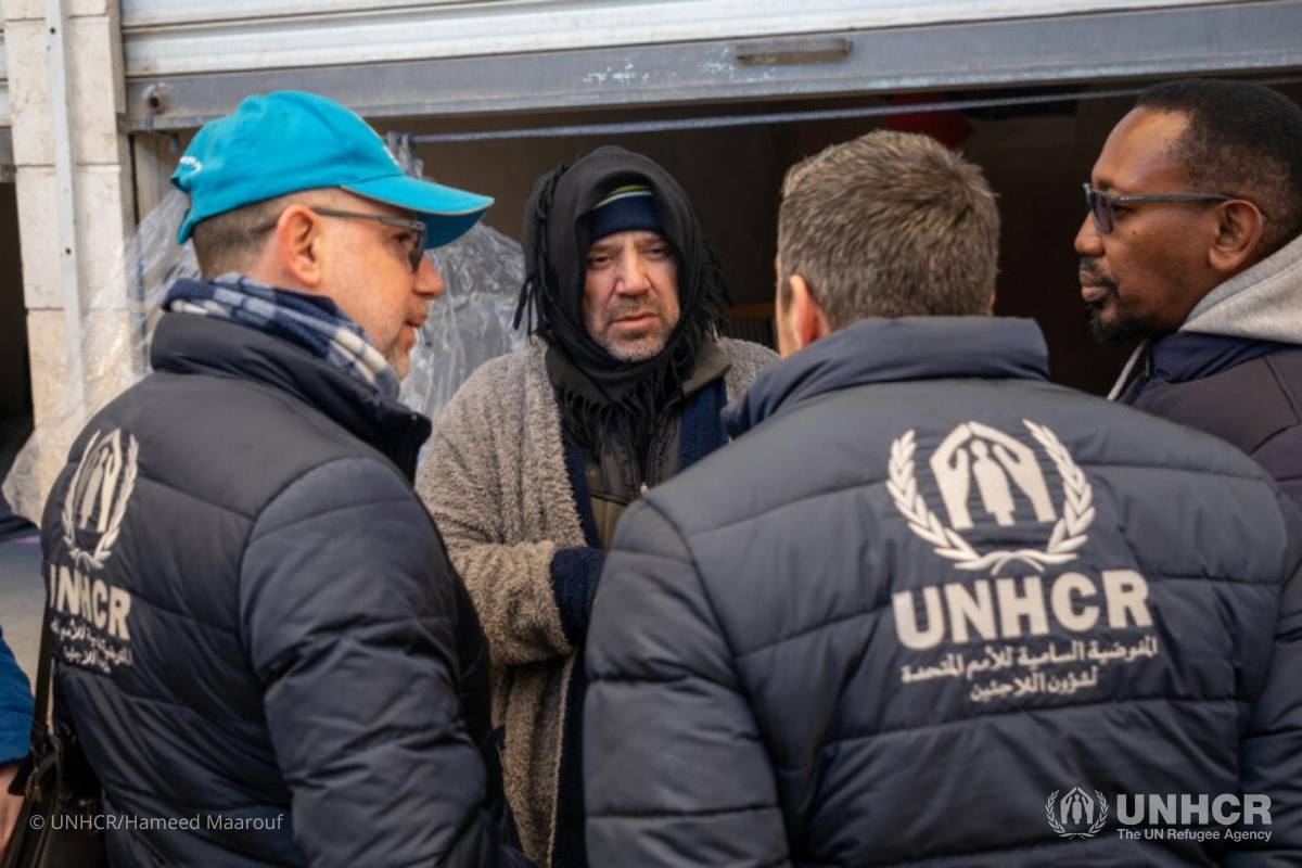 Mazen (center), a father of four from Aleppo whose home was damaged by the earthquakes, meets UNHCR staff outside the retail unit in Al-Harir souq where his family are staying.