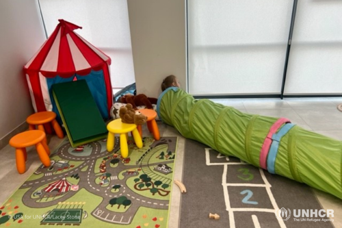 A young girl crawls through a lime green tunnel tube in the child-friendly space of a UNHCR-led Blue Dot Center in Warsaw, Poland.