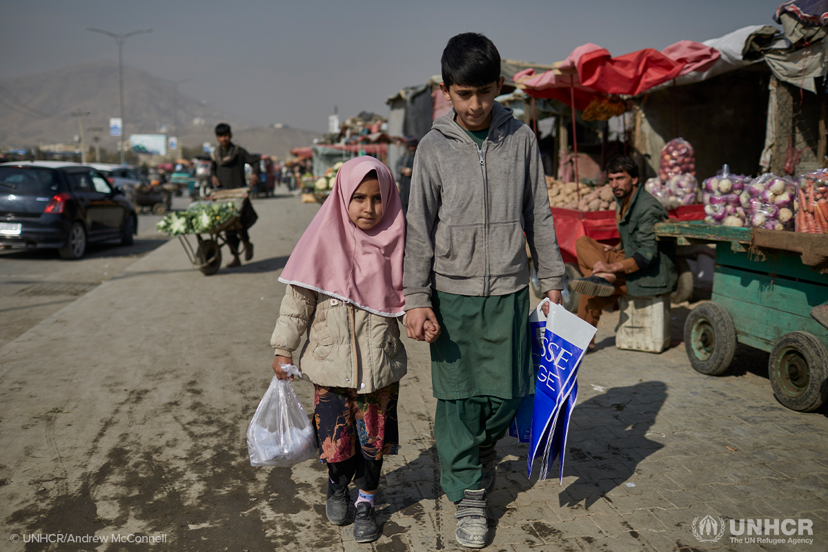 Displaced Afghan children Matiullah and Hajira hold hands as they walk through the market