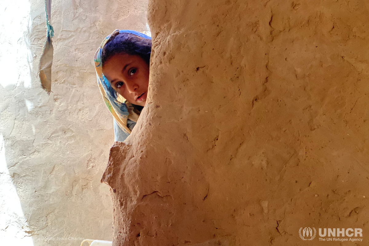 shaima peeks from behind the side of her house